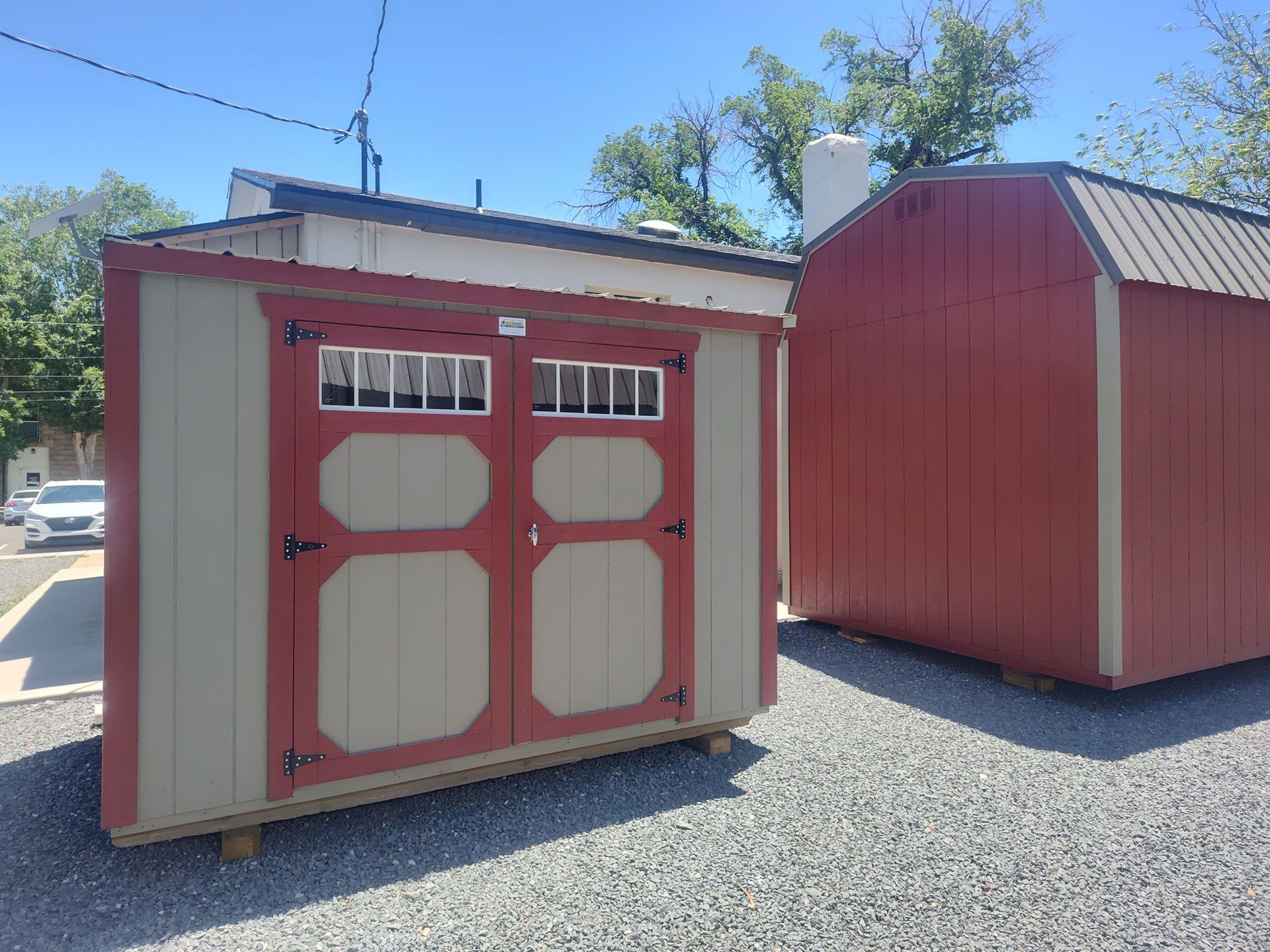 Two red-and-beige storage sheds on gravel under a bright blue sky