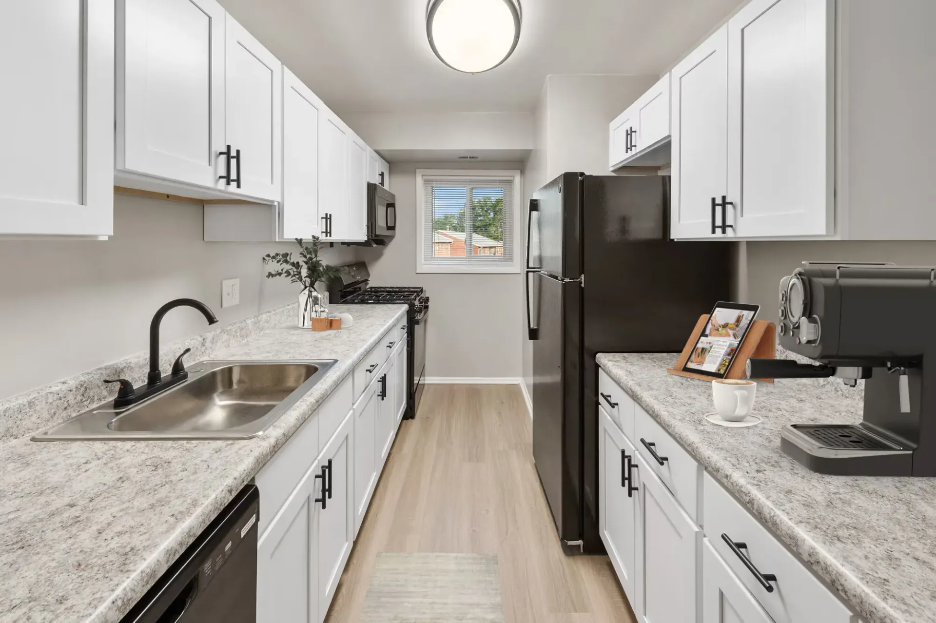 Narrow galley kitchen with white cabinets, stainless sink, black appliances, and a window at the far end at The Ridge Apartments in Hagerstown, MD