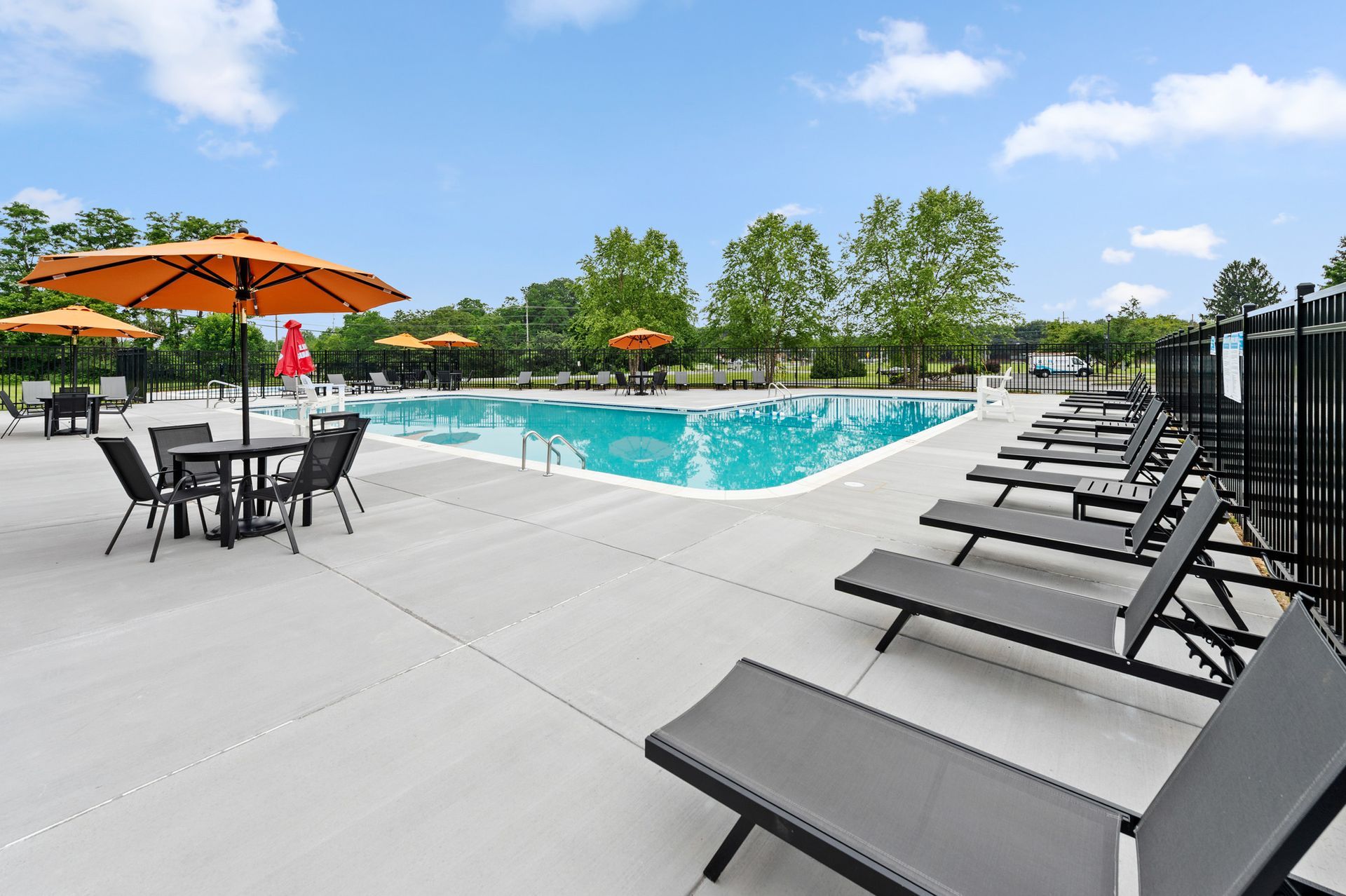 Outdoor pool area with orange umbrellas and black lounge chairs on a concrete deck at The Ridge Apartments in Hagerstown, MD