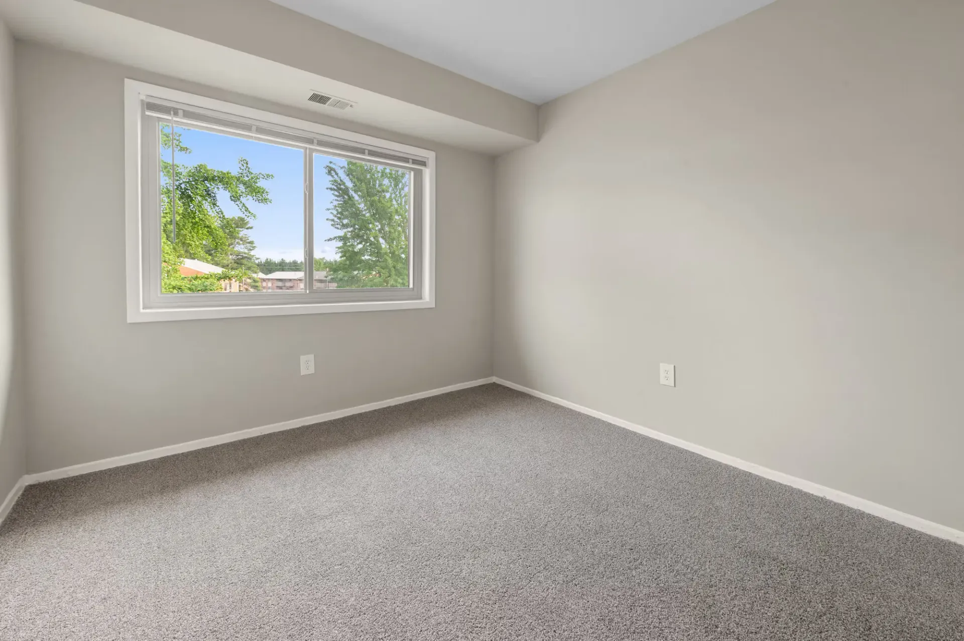 Empty bedroom with a large window, beige walls, and gray carpet at The Ridge Apartments in Hagerstown, MD