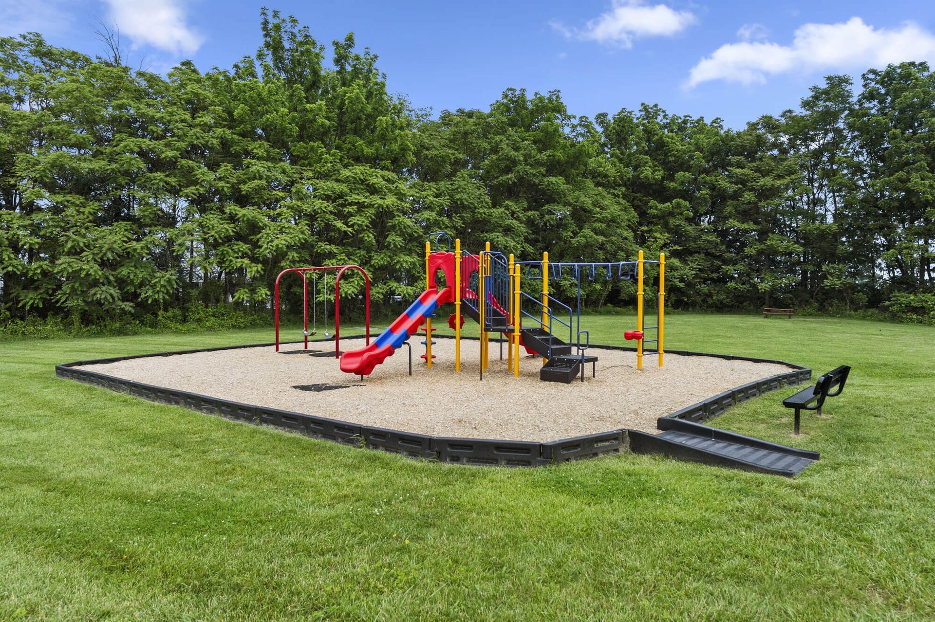 Playground equipment on a sandy surface with grass and trees around at The Ridge Apartments in Hagerstown, MD
