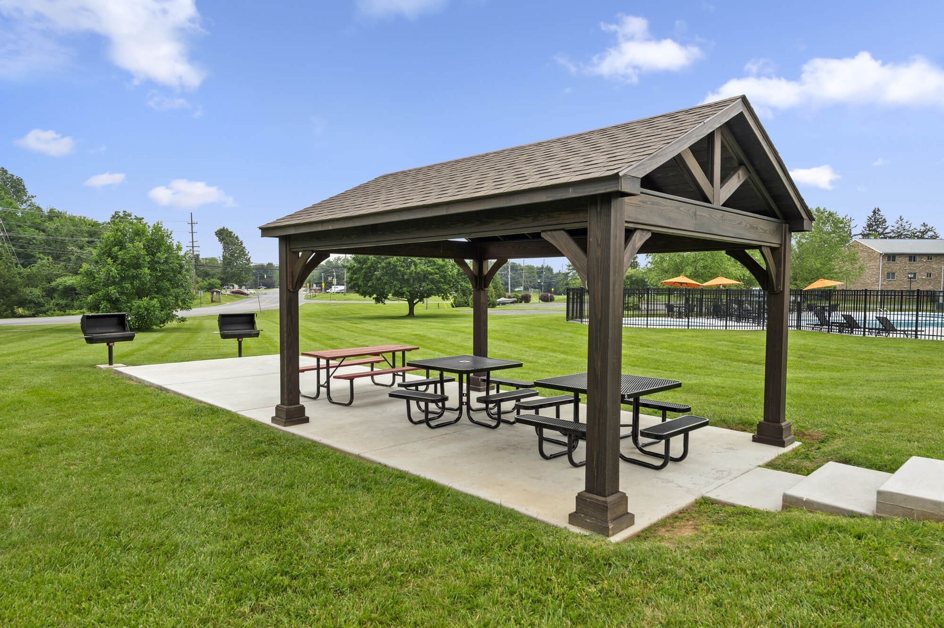 Wooden gazebo pavilion with picnic tables on a concrete pad in a grassy park near a pool at The Ridge Apartments in Hagerstown, MD