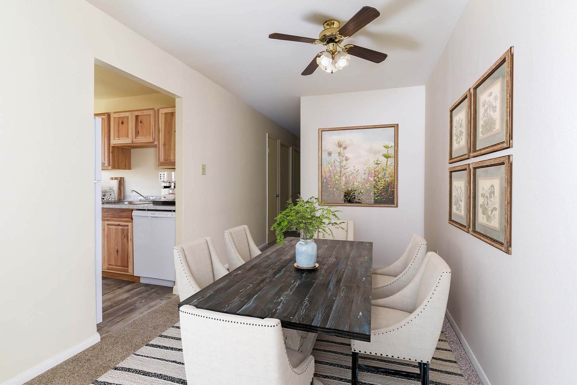 Dining area in a modern apartment with a dark wood table and cream upholstered chairs; kitchen doorway visible at The Ridge Apartments in Hagerstown, MD