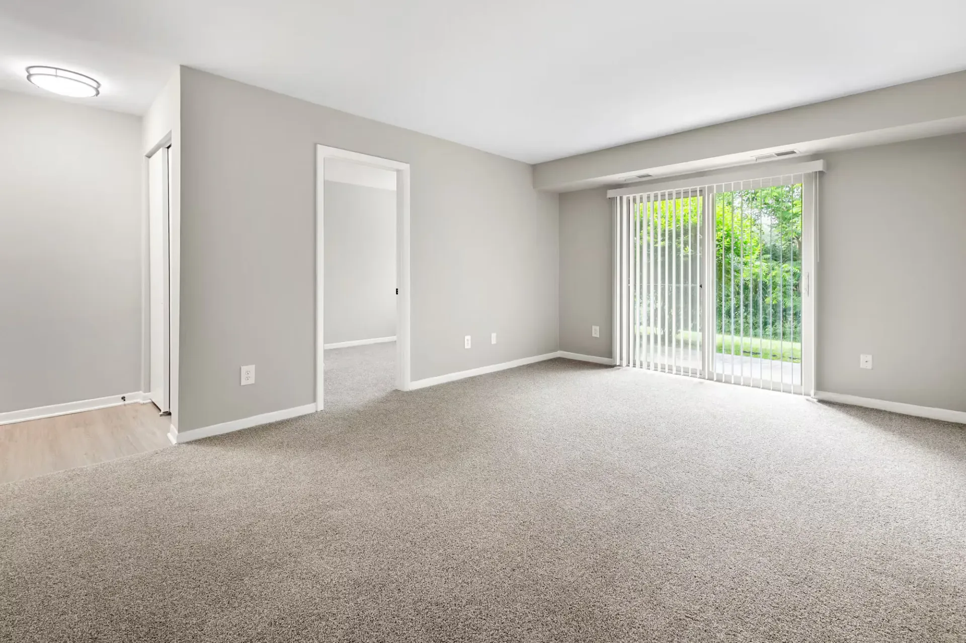 Bright living room with neutral gray walls, carpet, and sliding glass doors to the outdoors at The Ridge Apartments in Hagerstown, MD