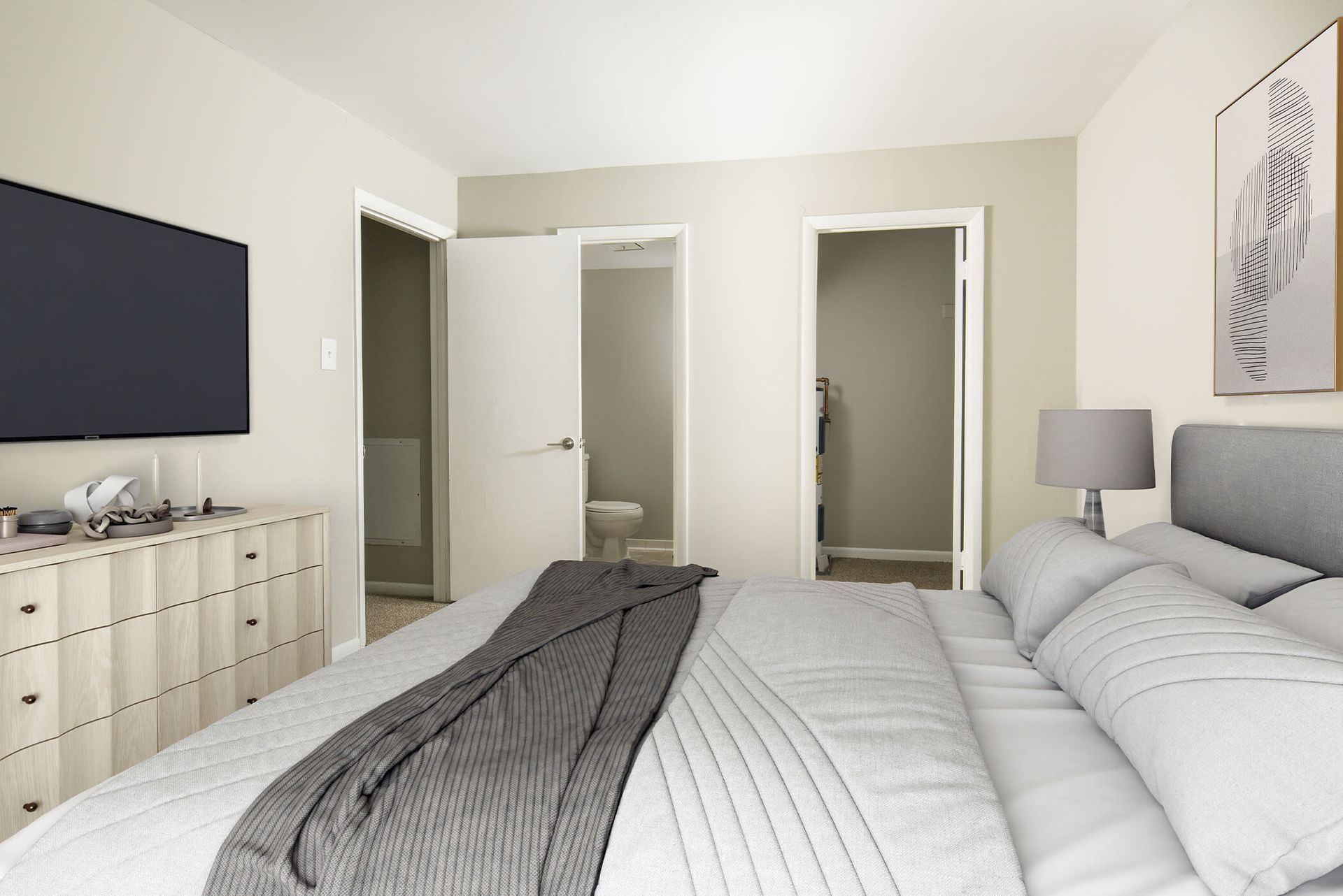 Bedroom in an apartment with a large bed, dresser, wall-mounted TV, and doors to the bathroom and closet at The Ridge Apartments in Hagerstown, MD