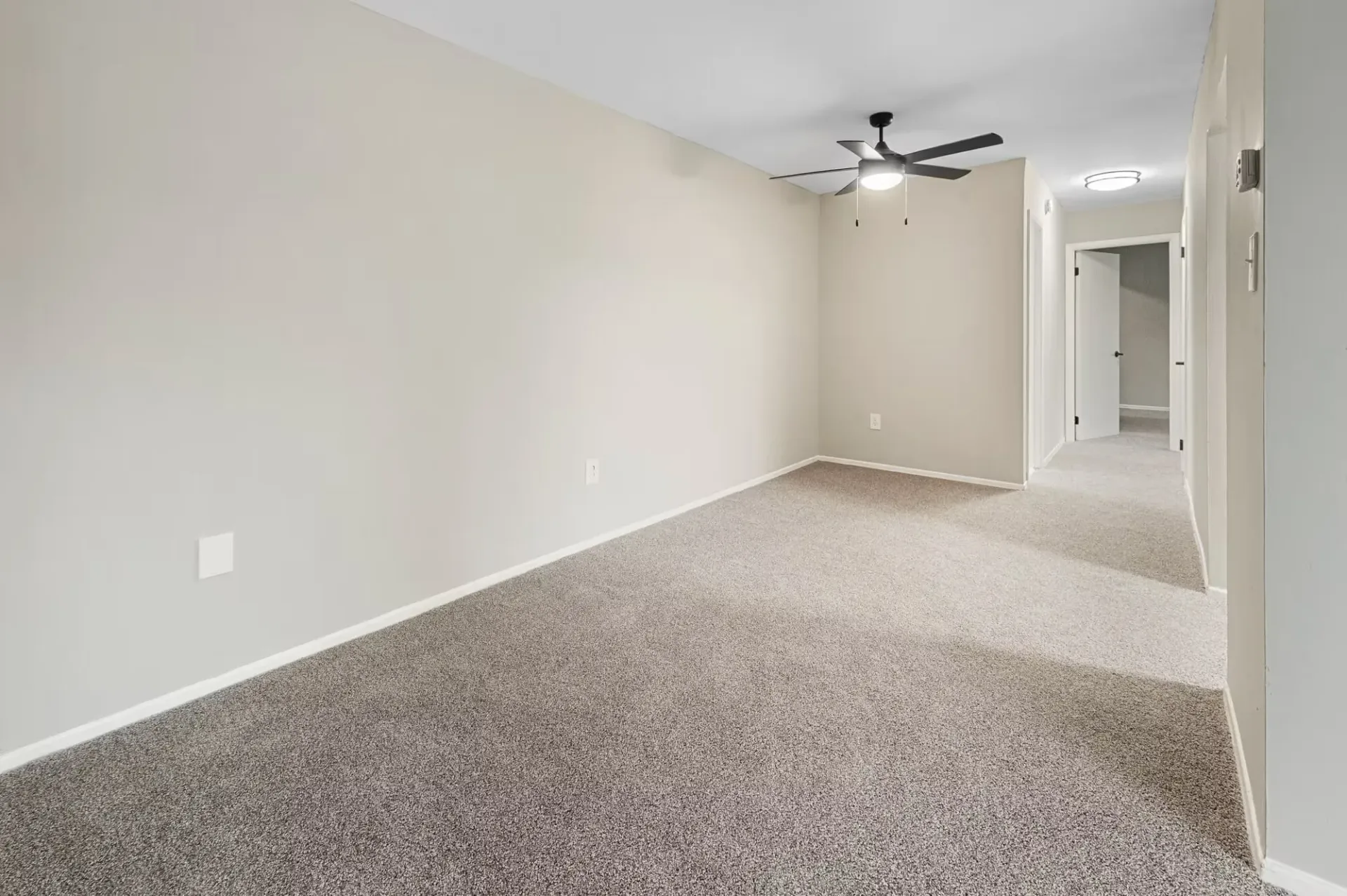 Empty living area in an apartment with beige walls, carpet, ceiling fan, and hallway at The Ridge Apartments in Hagerstown, MD
