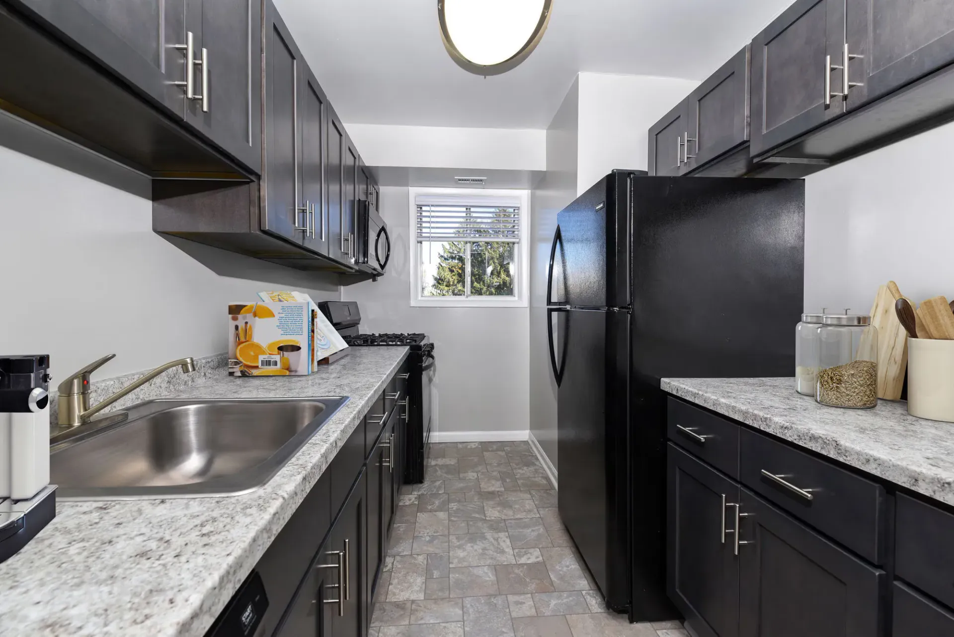 Narrow galley kitchen with dark cabinets, granite-like counters, black appliances, and a window at the far end at The Ridge Apartments in Hagerstown, MD