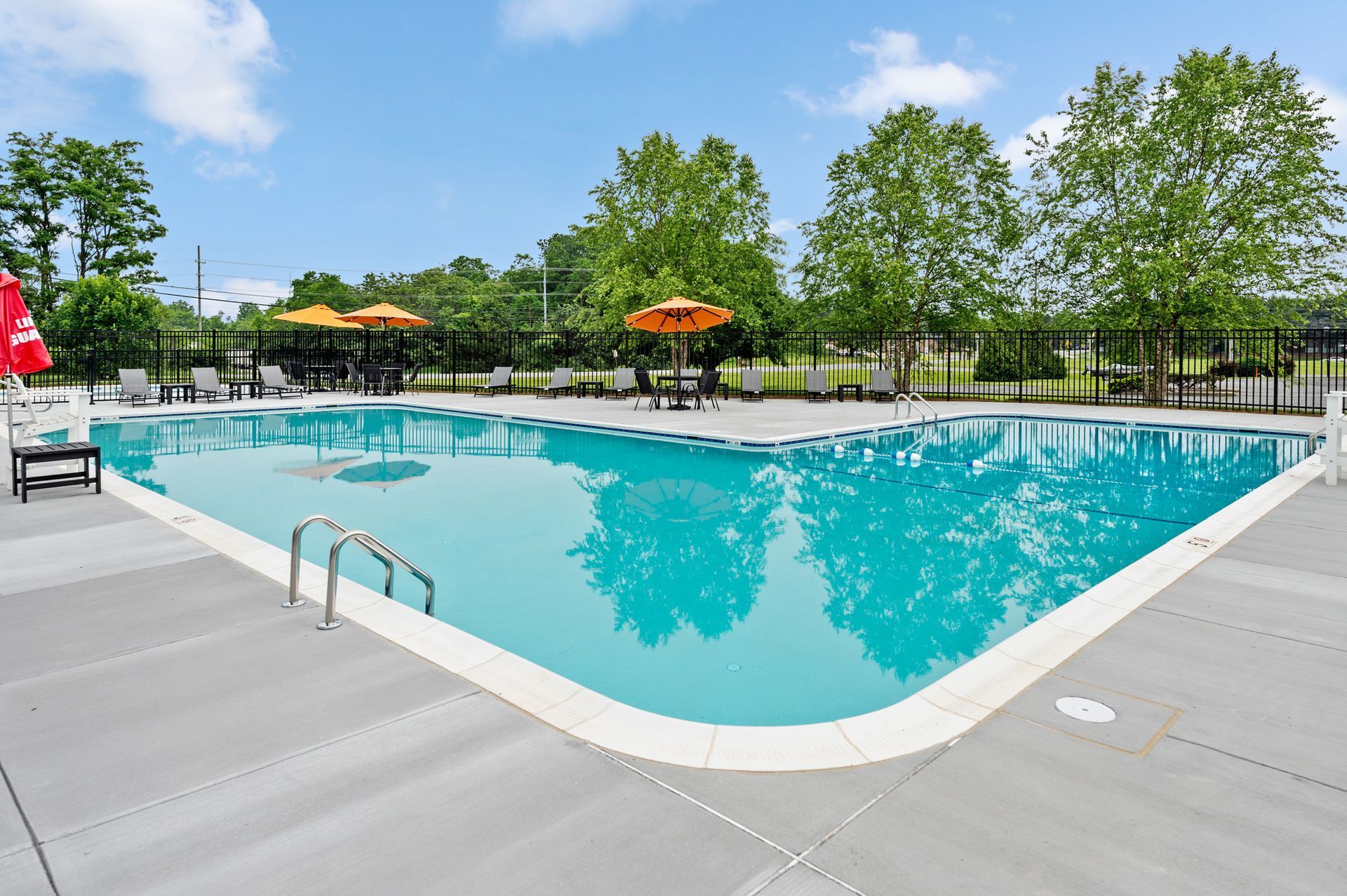 Outdoor community pool area with lounge chairs, orange umbrellas, and greenery at The Ridge Apartments in Hagerstown, MD