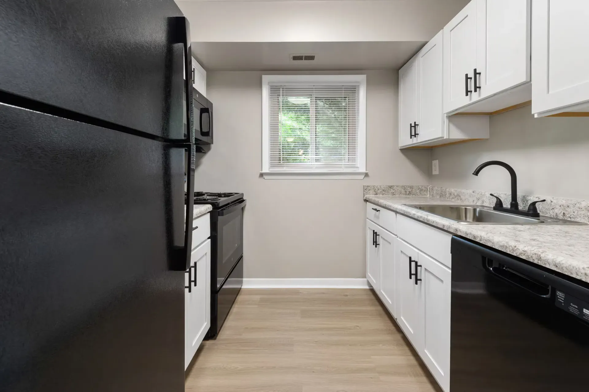 Narrow galley kitchen with white cabinets, black appliances, and a window above the sink at The Ridge Apartments in Hagerstown, MD
