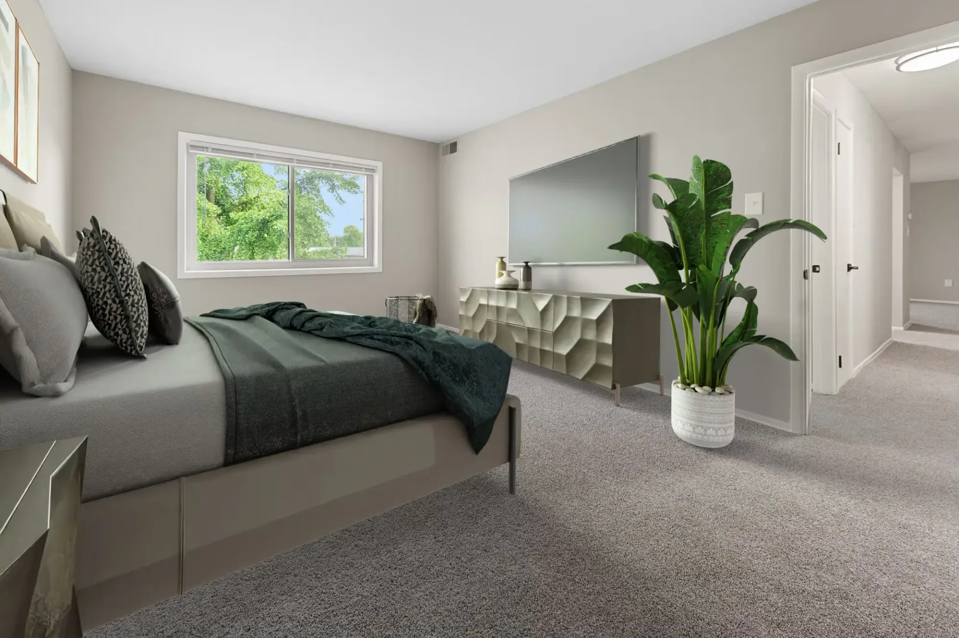 Modern apartment bedroom with a bed, dresser, wall-mounted TV, and large potted plant at The Ridge Apartments in Hagerstown, MD