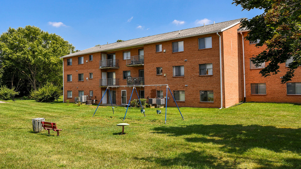 Exterior view of a brick apartment building with a grassy lawn and a playground at The Ridge Apartments in Hagerstown, MD