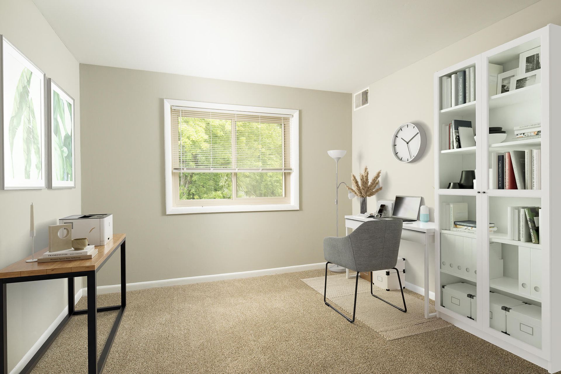 Home office in an apartment: white desk, gray chair, floor lamp, tall white bookcase, and a window with blinds at The Ridge Apartments in Hagerstown, MD