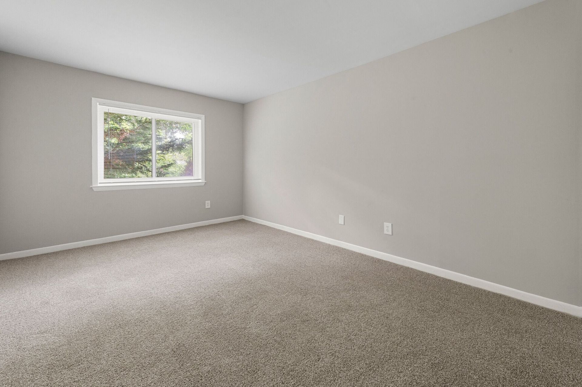 Empty beige carpeted bedroom with a window and outlets along the wall at The Ridge Apartments in Hagerstown, MD
