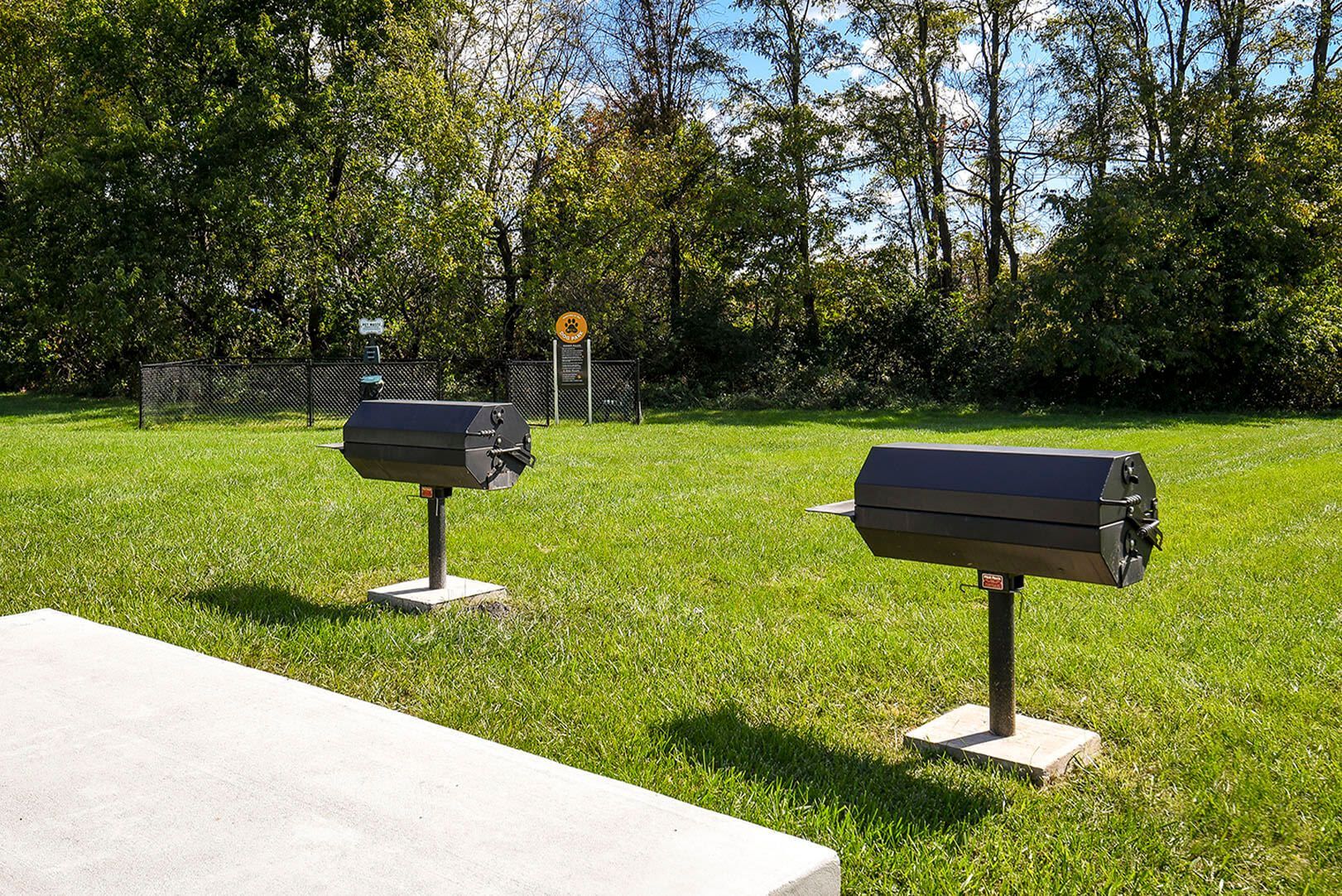 Two black outdoor grills on a grassy lawn with trees and fencing in the background at The Ridge Apartments in Hagerstown, MD