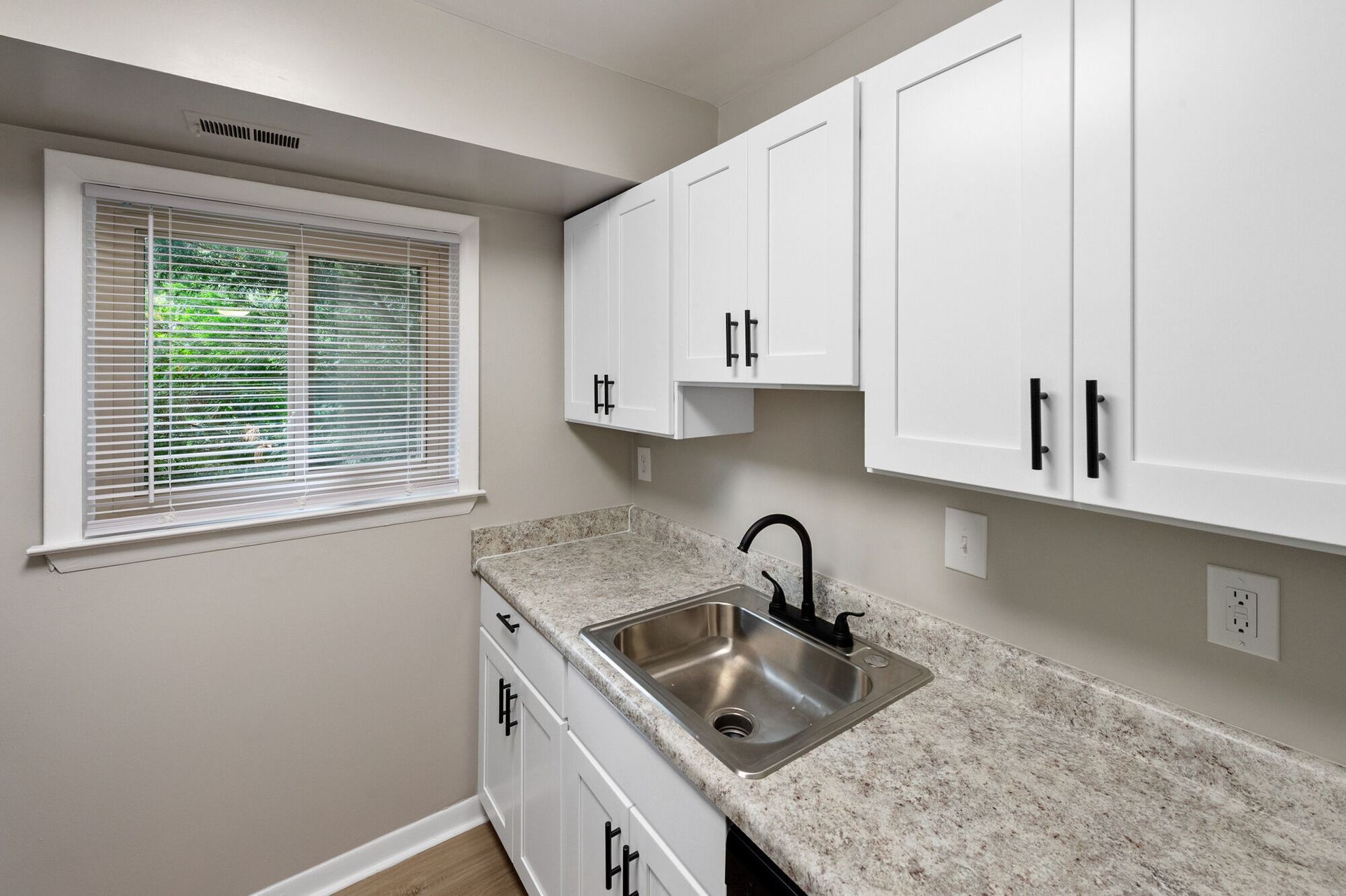 White kitchen with white cabinets, beige countertop, stainless steel sink, and a window with blinds at The Ridge Apartments in Hagerstown, MD