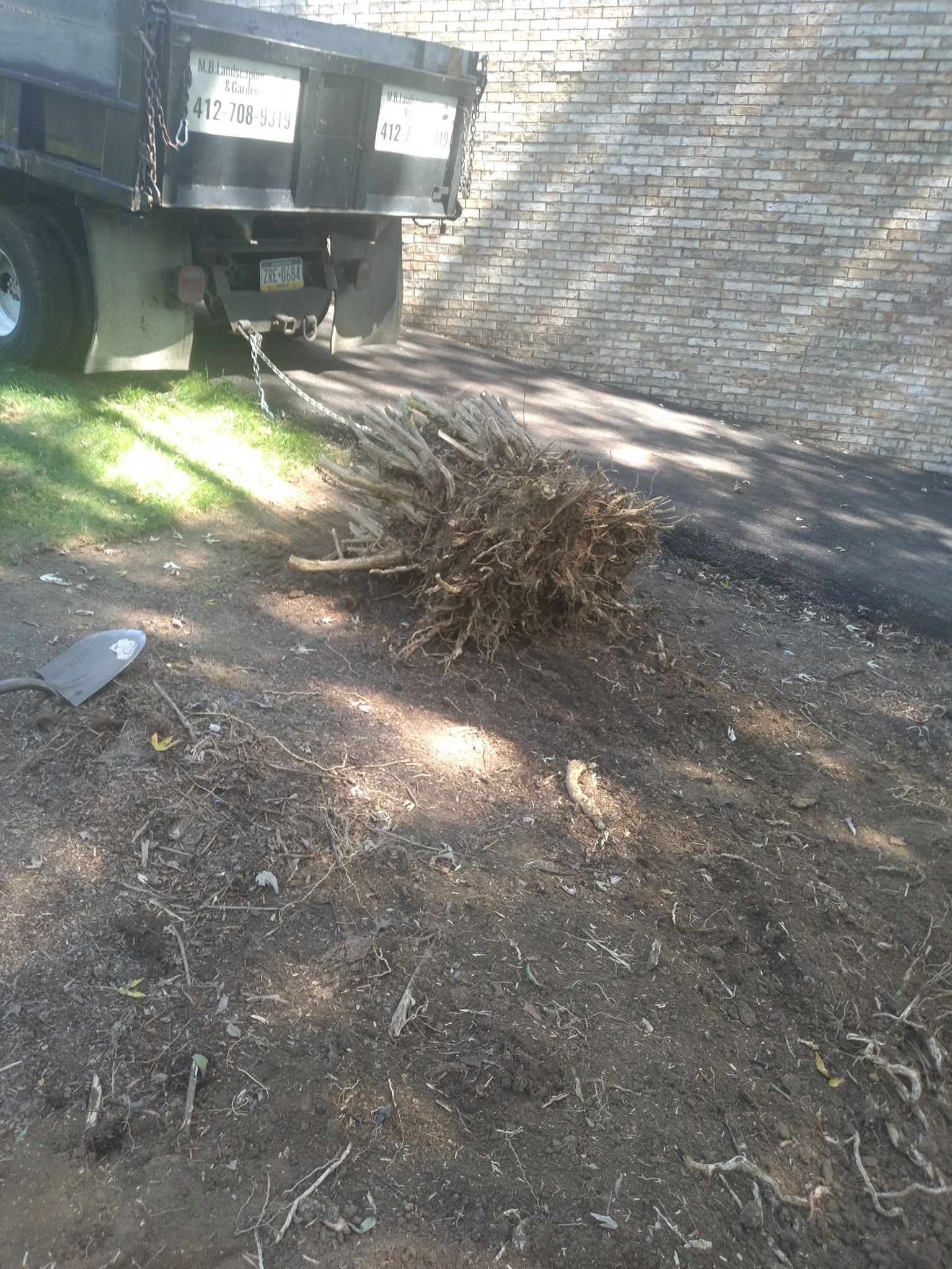 Truck by brick wall; debris pile on dirt; shovel on ground.