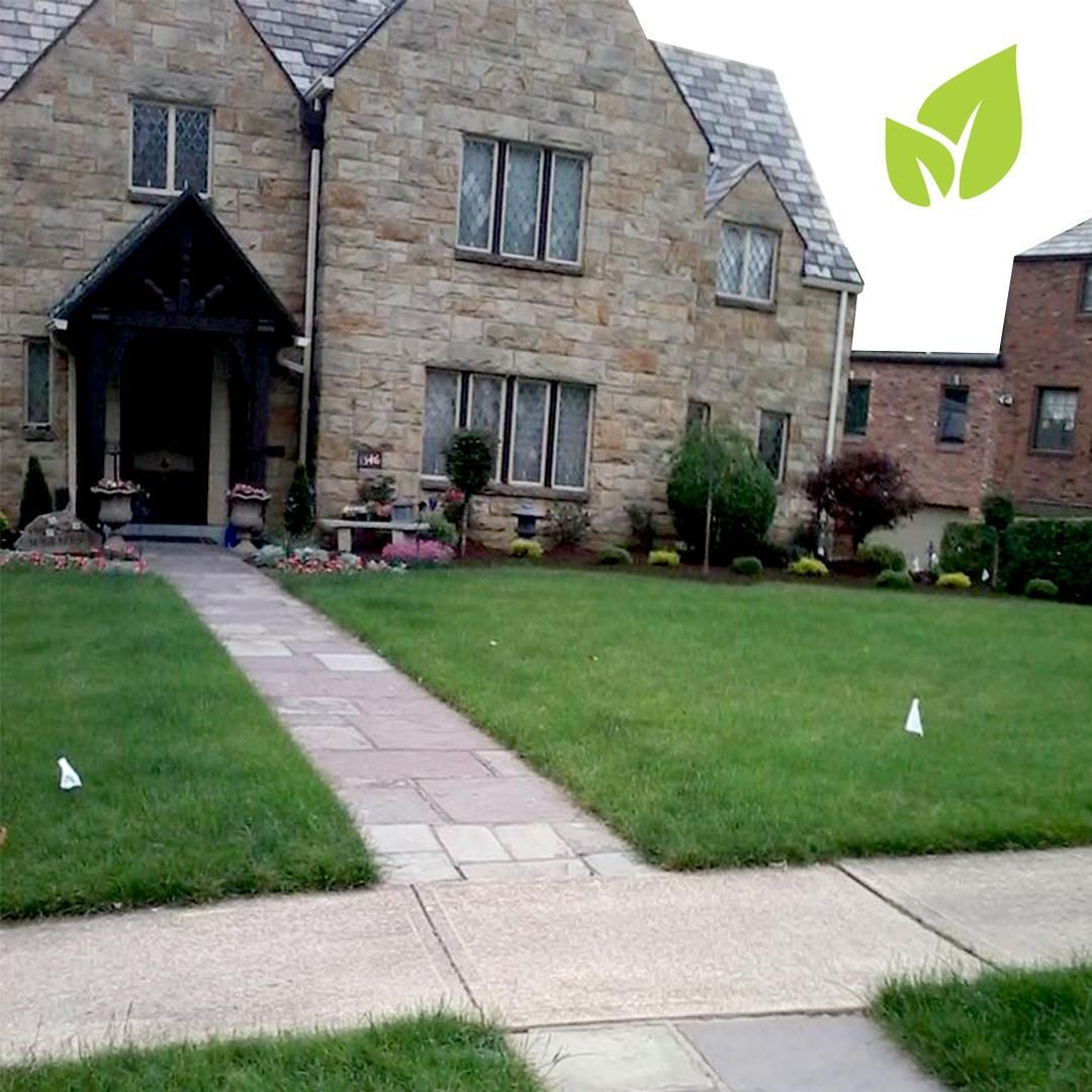 Stone house with a green lawn and paved walkway, with a leaf logo in the upper right corner.