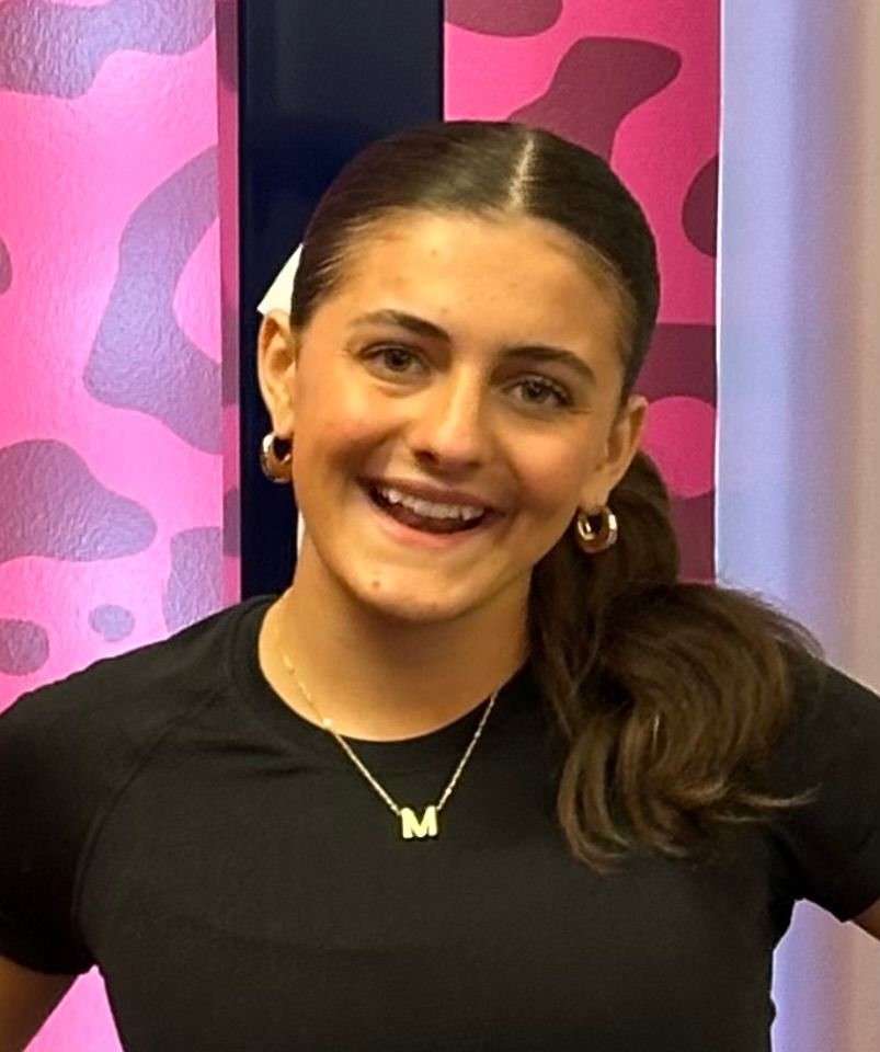 The girl is wearing a black shirt and a necklace with the letter m on it.