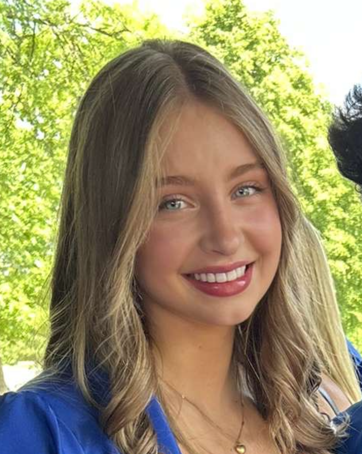 A young woman wearing a blue graduation cap and gown is smiling for the camera.