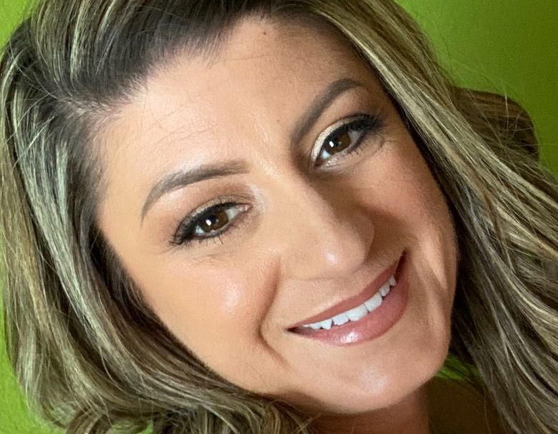 A close up of a woman 's face smiling in front of a green wall.