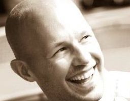 A bald man is smiling in a black and white photo.