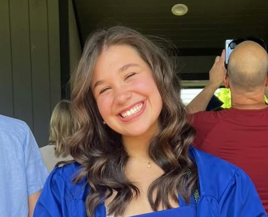 A woman in a blue cap and gown is smiling for the camera.