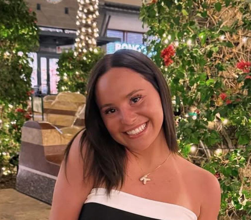 A woman is smiling in front of a christmas tree.