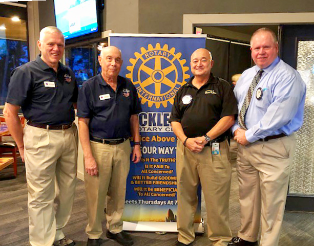 Four men in front of a Rotary Club banner; they are smiling in a restaurant setting.