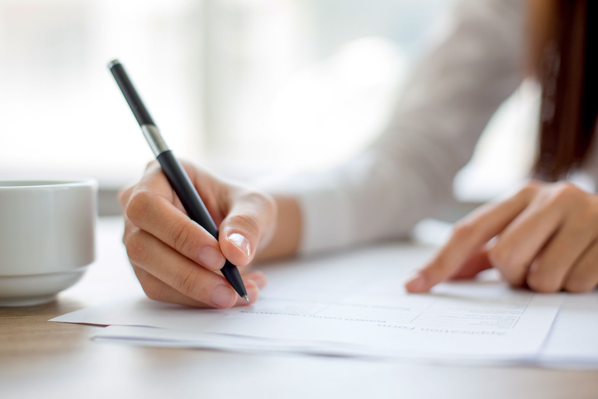 A woman is writing on a piece of paper with a pen.