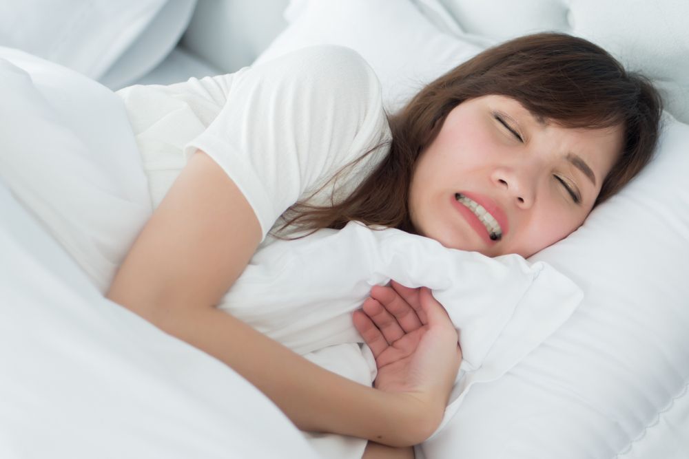 Woman in bed, face contorted in pain, clutching a pillow.