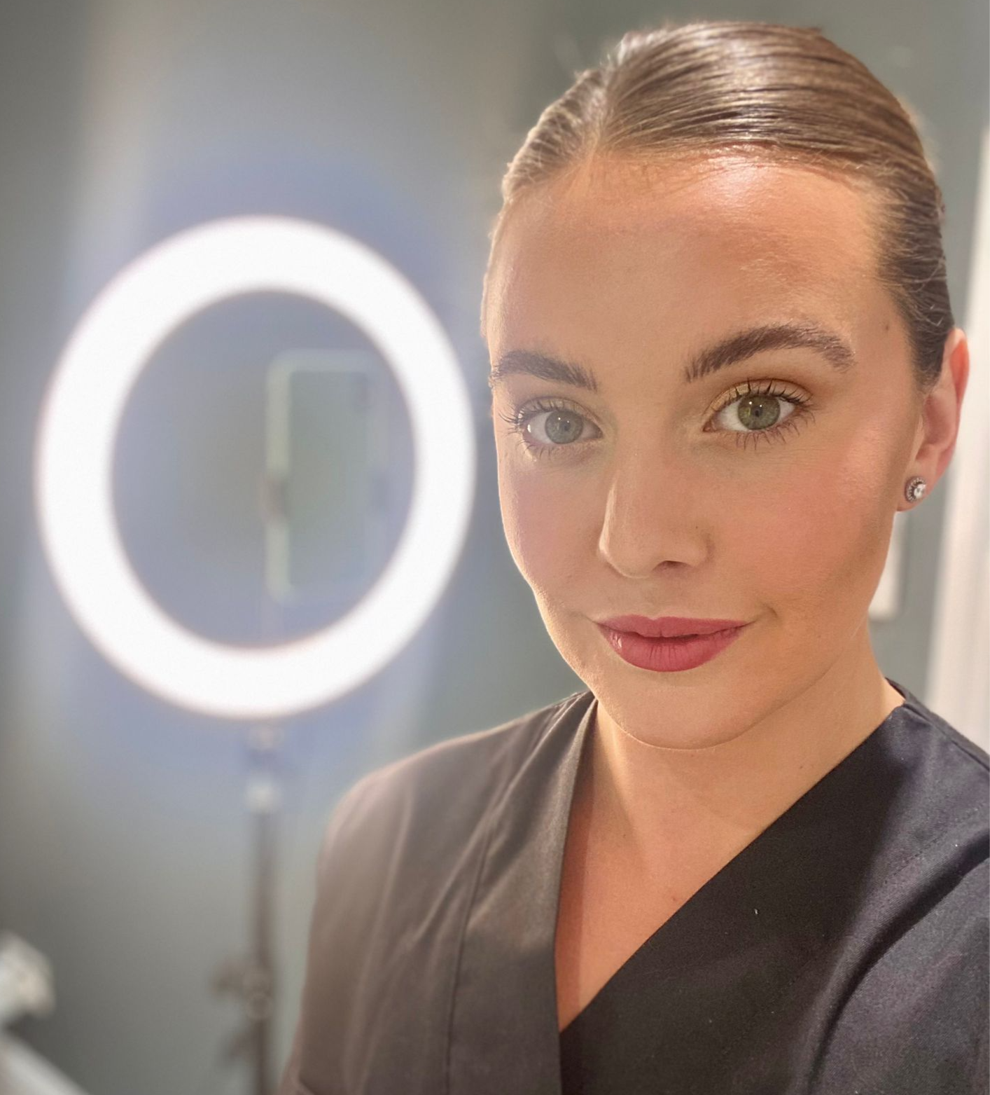 A woman is taking a selfie in front of a ring light.