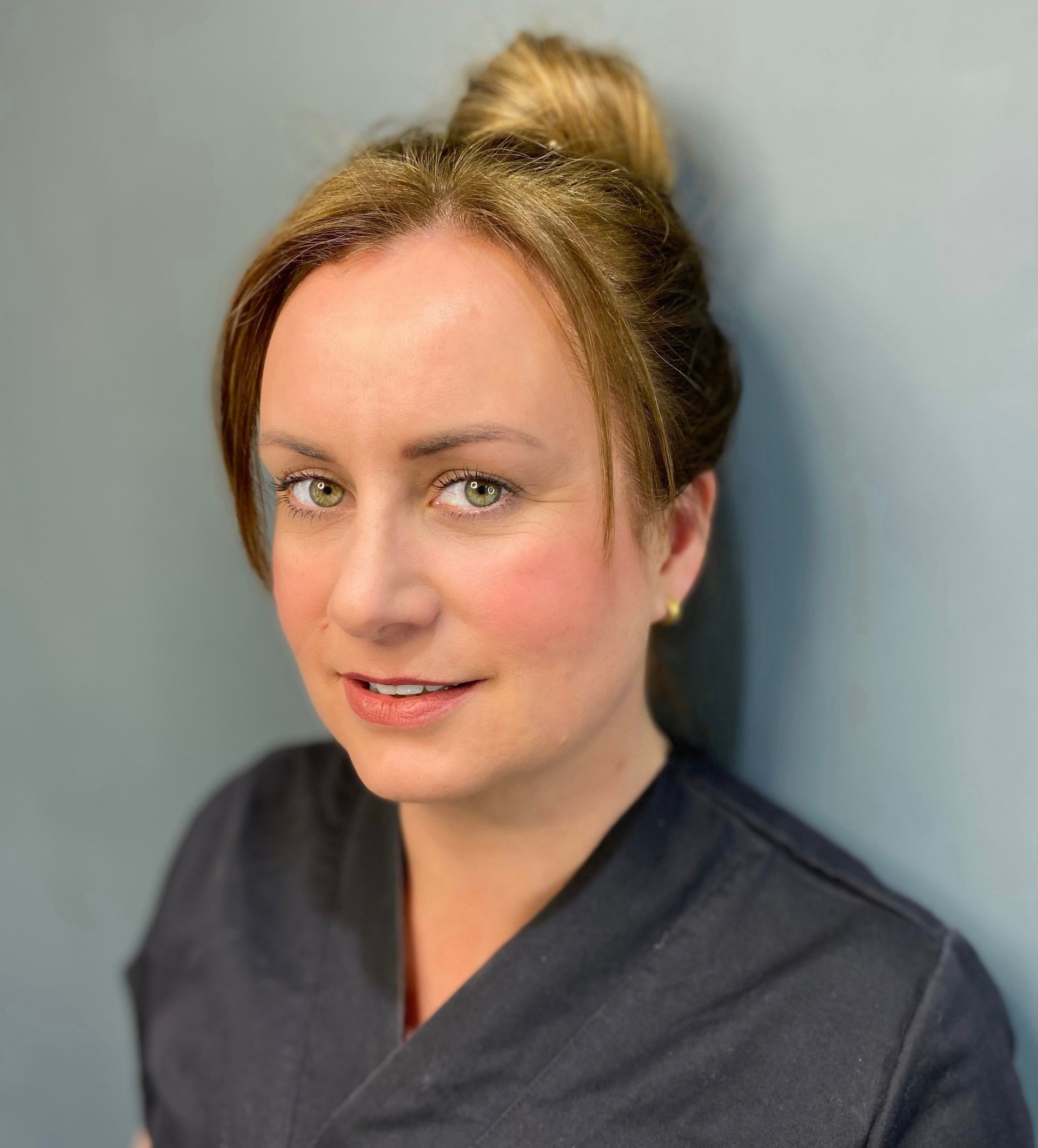 A woman in a black scrub is smiling for the camera.