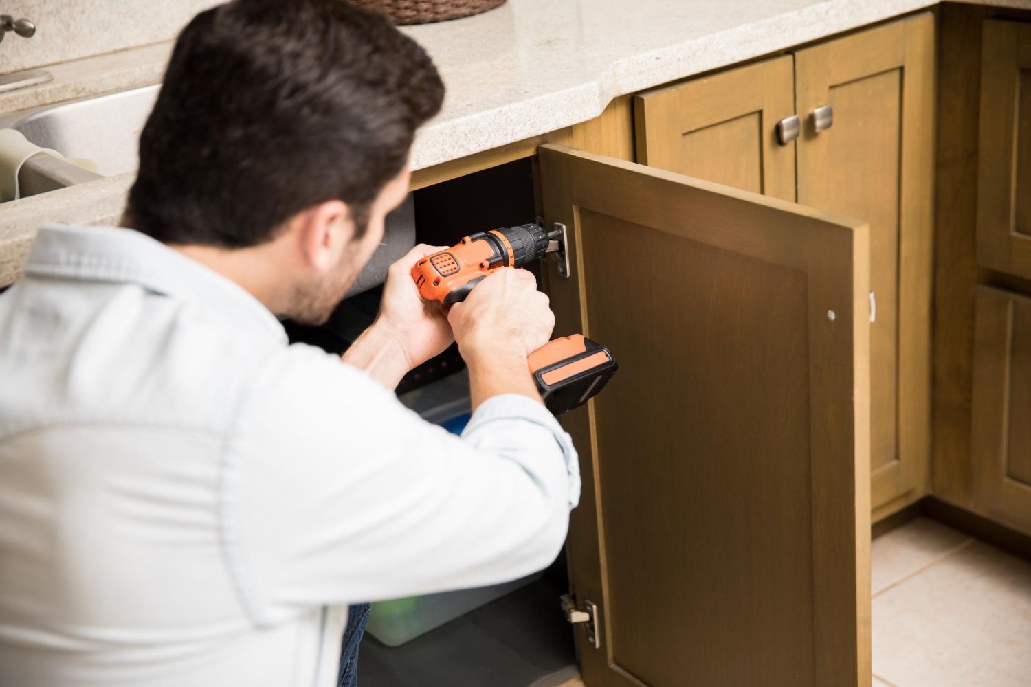 A man is using a drill to fix a cabinet in a kitchen.