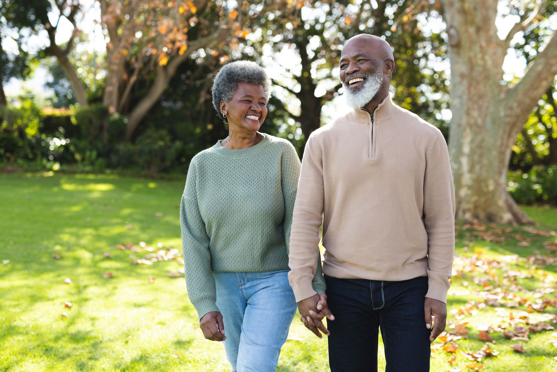 Two people walking together on a sunny grassy path in a park, smiling and holding hands.