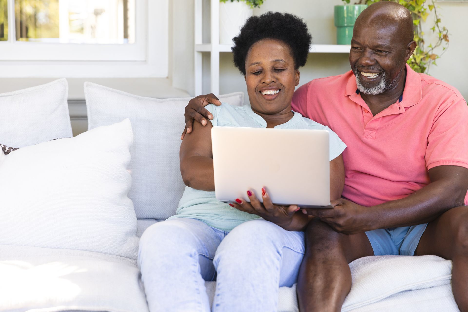 Couple smiling on a couch, looking at a laptop together in a bright living room