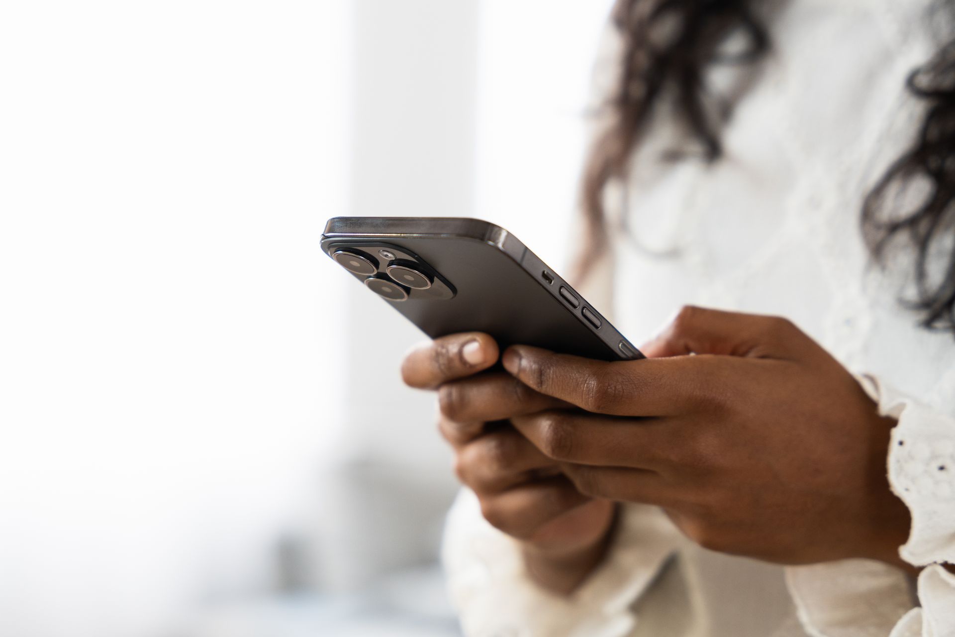 Person in a white sweater using a smartphone, close-up against a blurred background