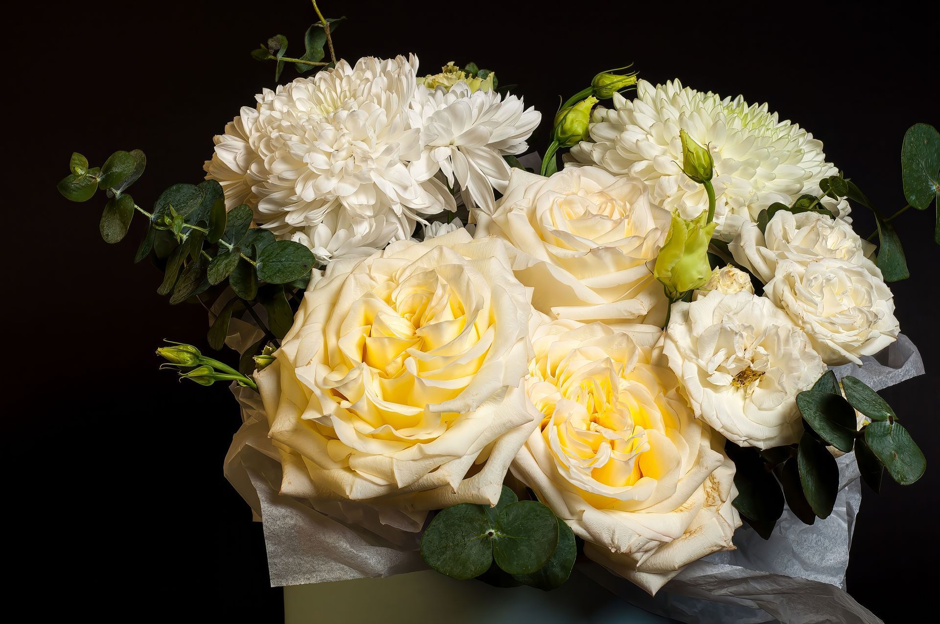 Bouquet of cream and white roses and chrysanthemums with green leaves on a dark background