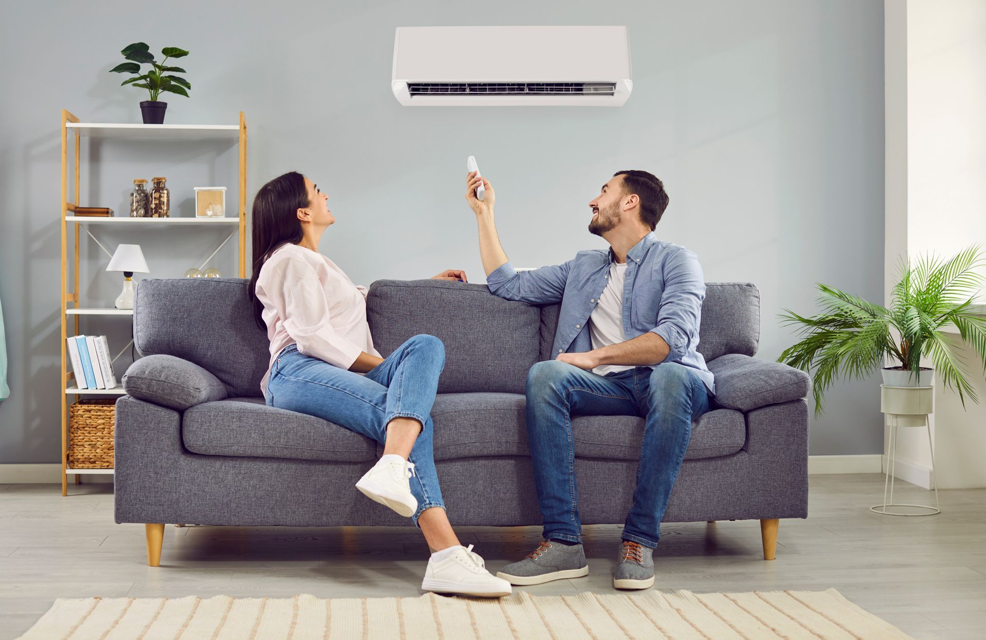 A couple is turning on the air conditioner and sitting on the sofa at home.