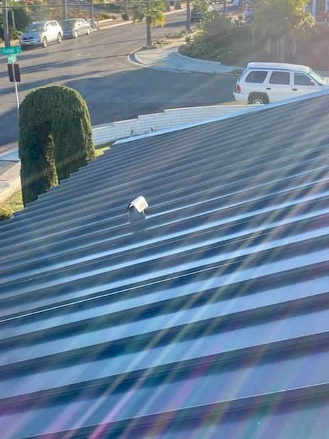 Metal roof with a small vent, street in the background. Sunny day.