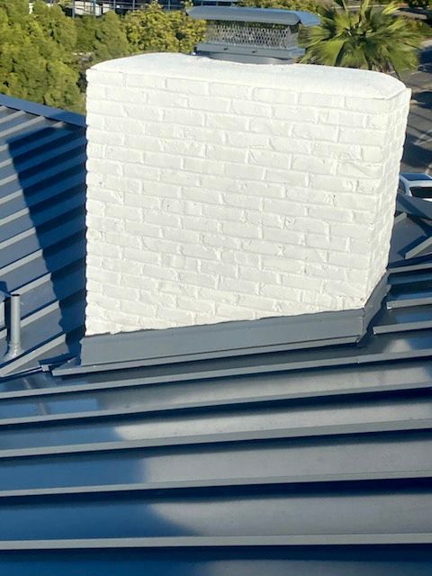 White brick chimney on a blue metal roof, outdoors.
