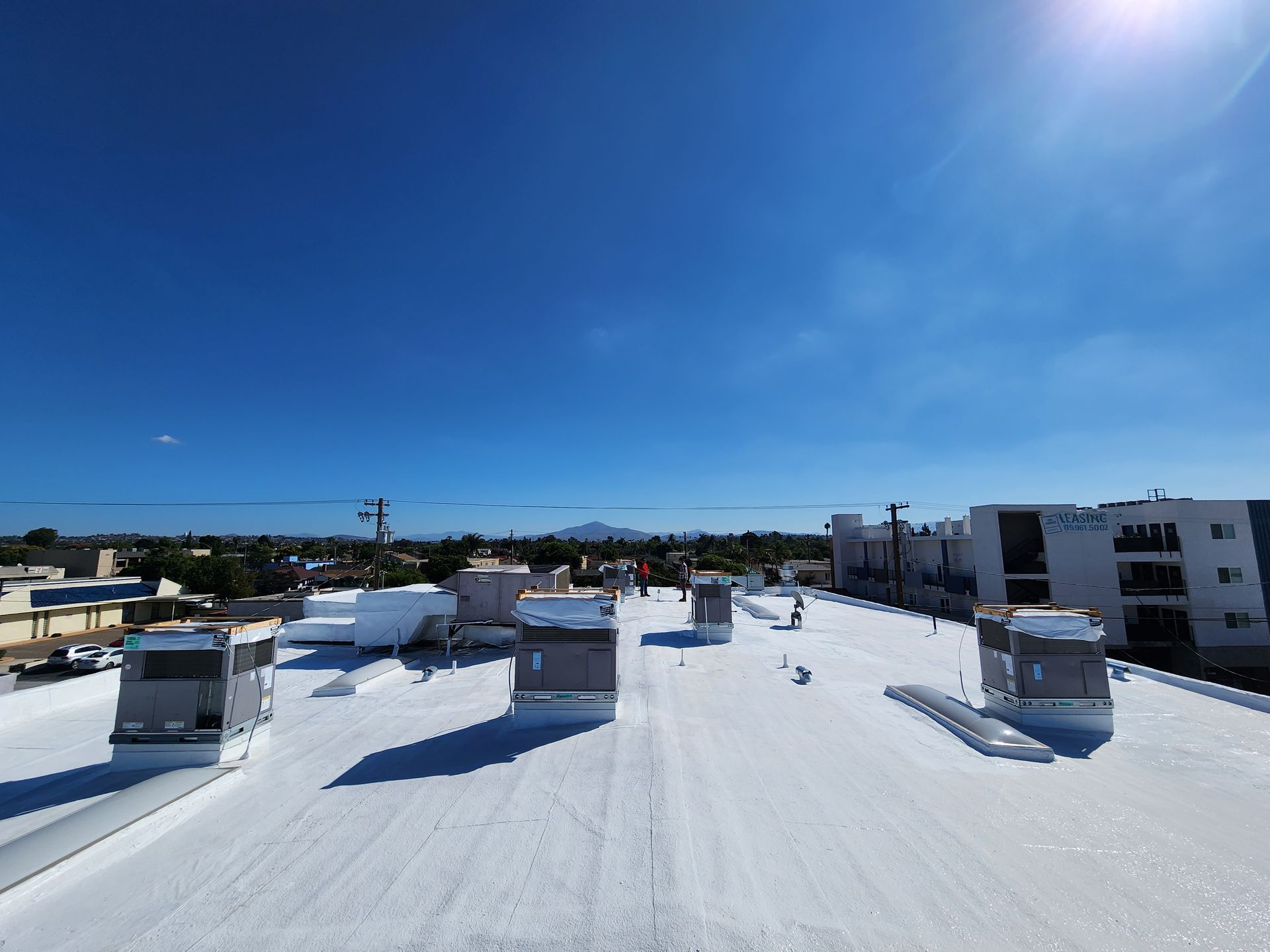 White roof with HVAC units under a blue sky; workers present.