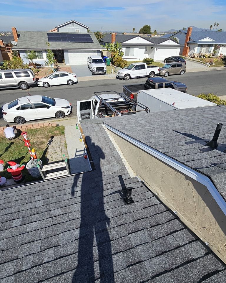 Rooftop view of houses and street. Workers on roof next to a truck. Clear sky, sunny day.