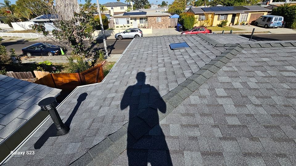 Shadow on a gray shingle roof overlooking a neighborhood with houses and cars.