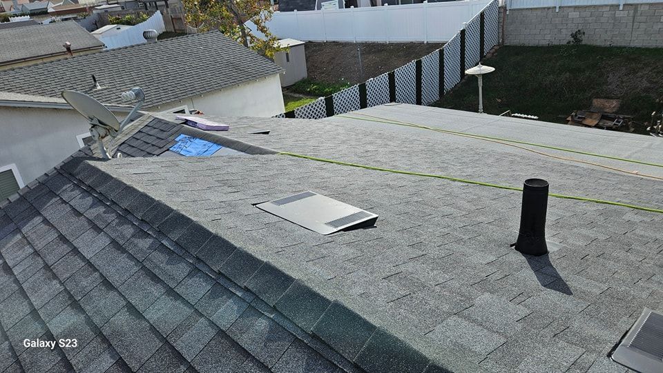 Gray asphalt shingle roof with vents, a satellite dish, and a wire against a sunny background.