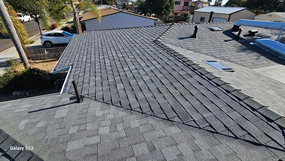 Overhead view of a gray shingled roof on a residential building, with several vents and a car parked in the street.