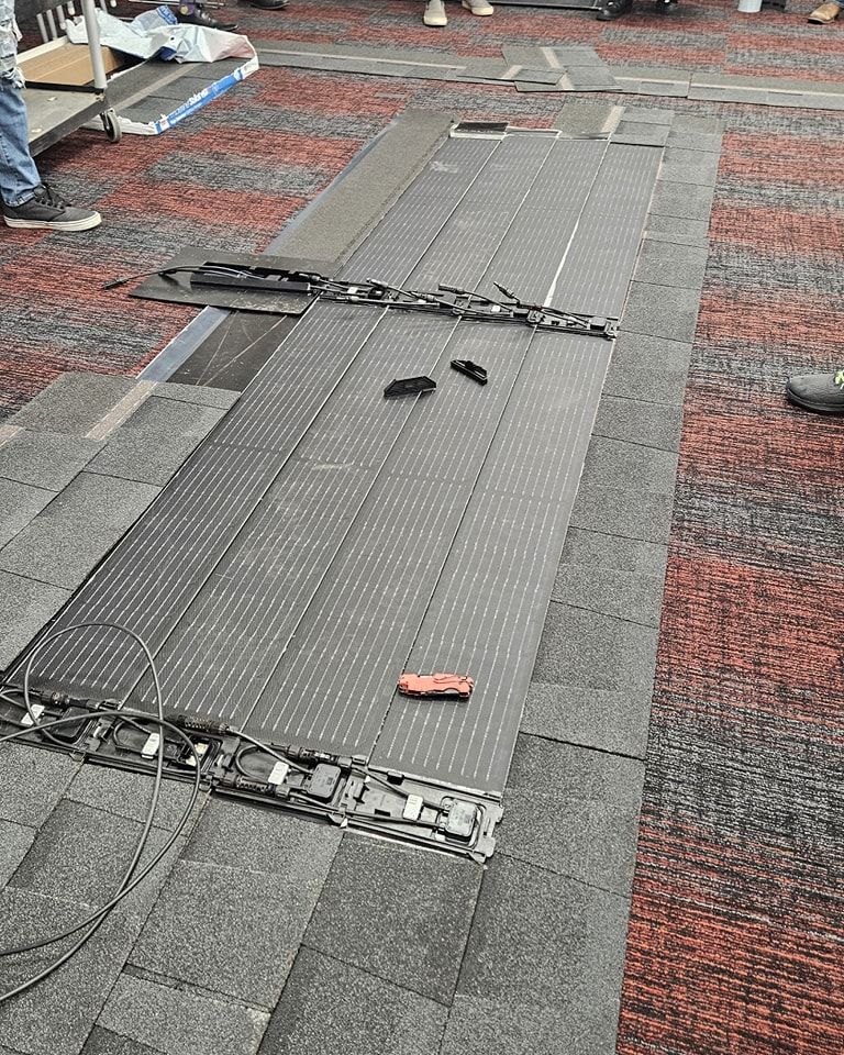 Solar roof tiles laid on a shingled roof for demonstration. connected by wires, on a reddish-brown and gray roof.