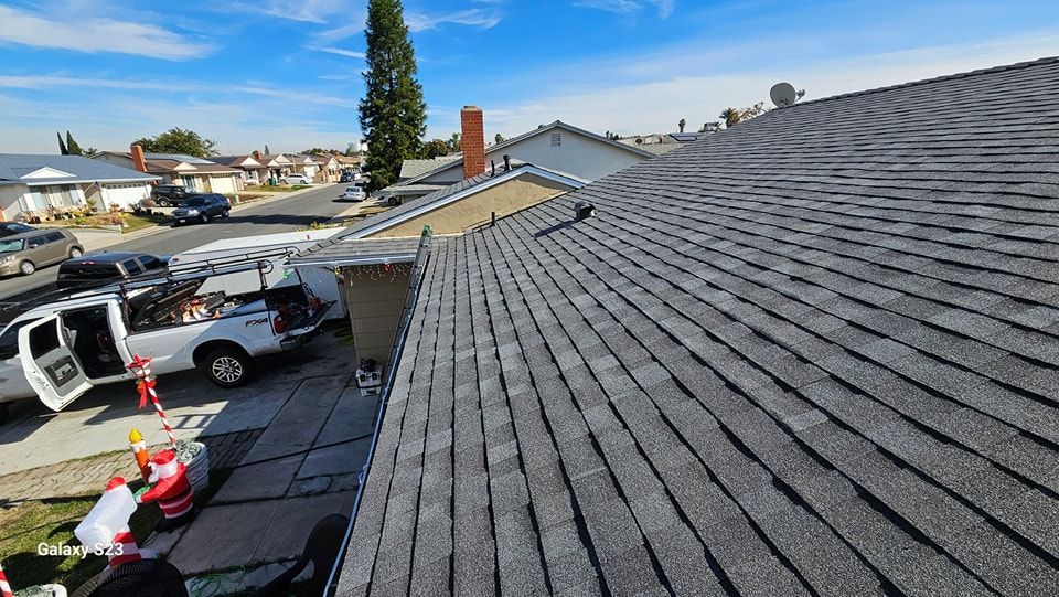 View of a shingled roof with a chimney, a truck and equipment are on the ground in front.