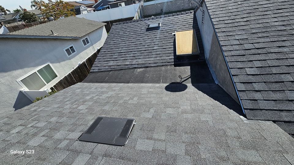Overhead view of several rooftops with asphalt shingles, vents, and a partially visible white building.