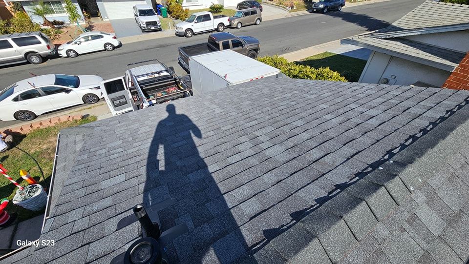 Shadow of a person on a dark gray shingled roof, view includes street with parked cars and a utility truck.