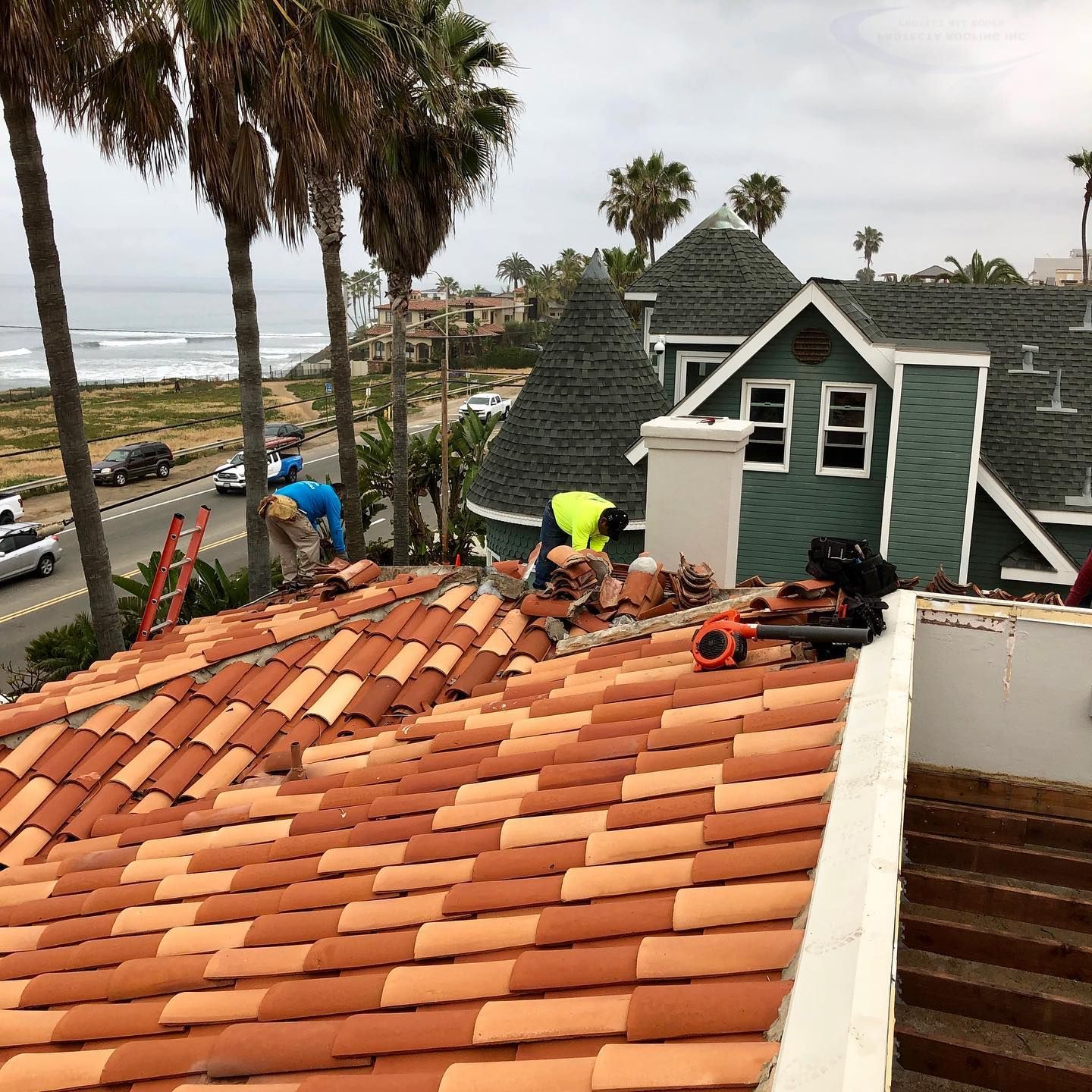 Roofers working on a clay tile roof near the ocean, some wearing safety vests.